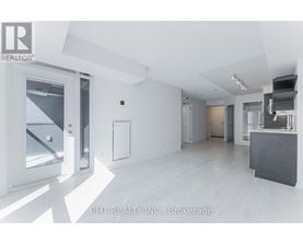 A spacious, empty room with white walls and flooring, and a large window on the left side.