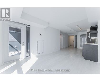 A spacious, empty room with white walls and flooring, and a large window on the left side.