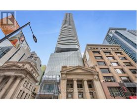 A tall building with a curved glass facade stands in front of a row of older buildings.