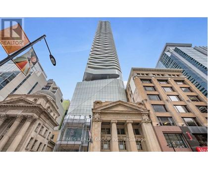 A tall building with a curved glass facade stands in front of a row of older buildings.
