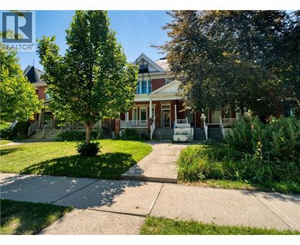 A house with a red brick exterior and a white picket fence is surrounded by greenery.