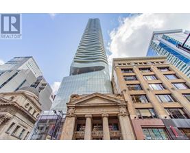 A tall glass building stands in front of a historic building with a brokerage logo on it.