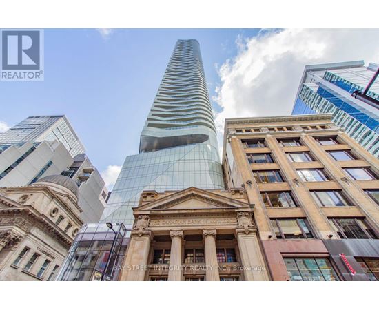 A tall glass building stands in front of a historic building with a brokerage logo on it.