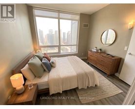 A bedroom with a large bed, a nightstand, and a window overlooking a cityscape.