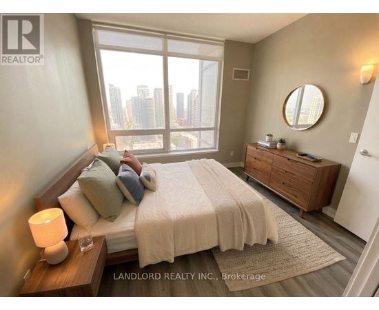 A bedroom with a large bed, a nightstand, and a window overlooking a cityscape.