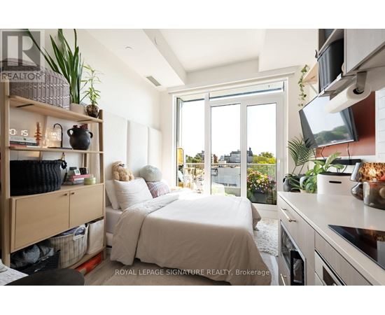 A well-lit bedroom with a large bed and a kitchen area with a stove top oven.