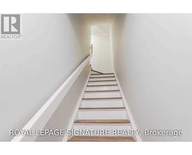 A white hallway with a staircase and a logo for Royal LePage Signature Realty in Brokerage.