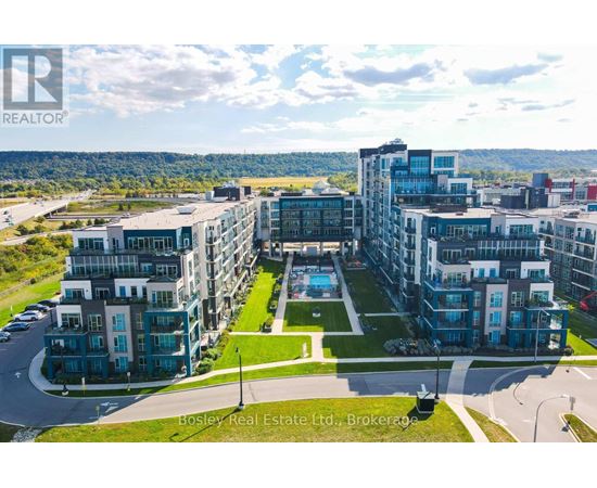 A large, modern apartment complex with a pool in the center, surrounded by greenery and a clear sky.