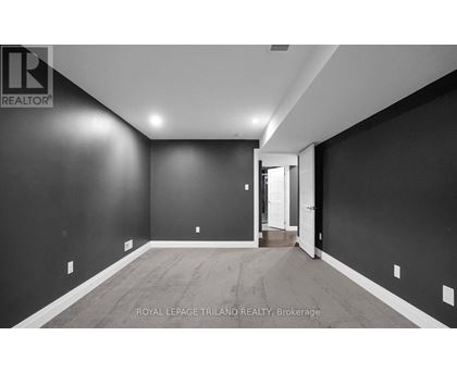 A spacious room with dark walls and wooden flooring, with a doorway leading to another room.
