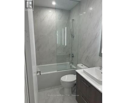 A white toilet is in a bathroom with a marble wall.