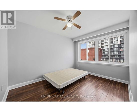 A bedroom with a bed, ceiling fan, and a window overlooking a building.