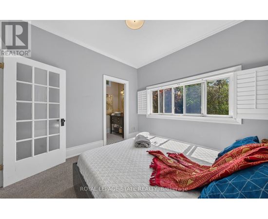 A bedroom with a bed, pillows, and blankets in front of a window with white shutters.