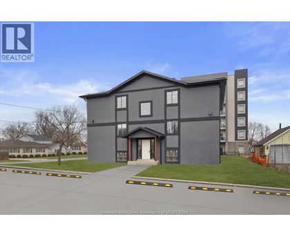 A modern grey building with a large front yard and a clear blue sky.