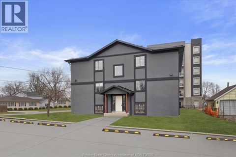 A modern grey building with a large front yard and a clear blue sky.