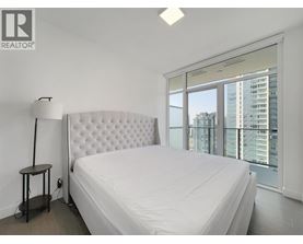 A bedroom with a large bed and a city view through the window.