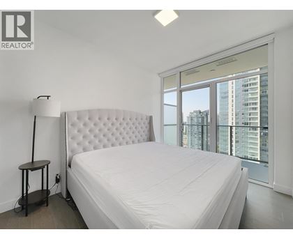 A bedroom with a large bed and a city view through the window.