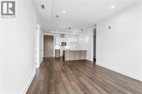 A spacious living room with wood flooring and white walls.