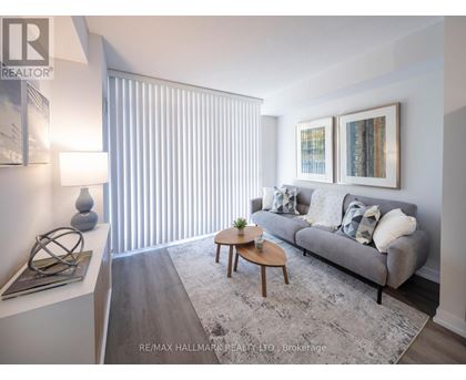 A living room with a grey couch, a coffee table, and a large window with blinds.