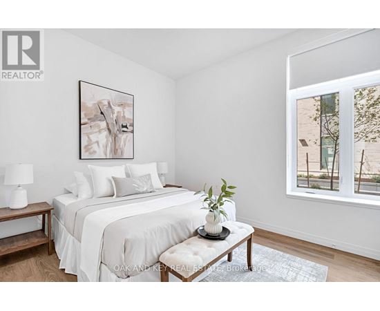 A bedroom with a large bed, a nightstand with a lamp, and a framed picture on the wall.