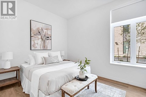 A bedroom with a large bed, a nightstand with a lamp, and a framed picture on the wall.