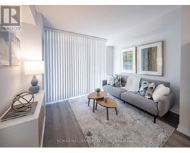 A living room with a grey couch, a coffee table, and a large window with blinds.