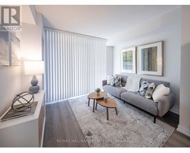 A living room with a grey couch, a coffee table, and a large window with blinds.