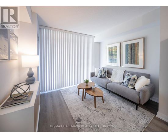 A living room with a grey couch, a coffee table, and a large window with blinds.