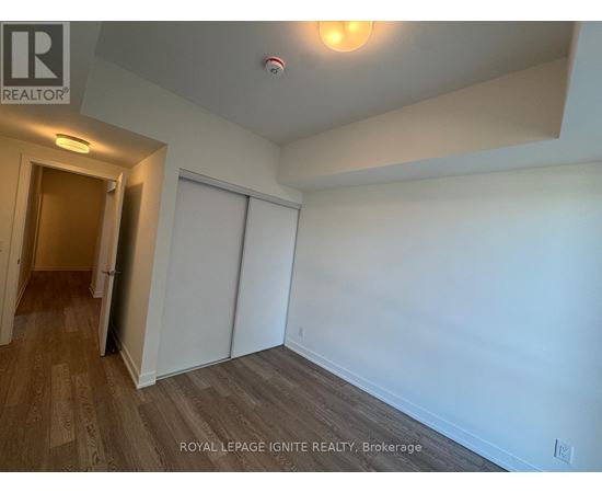 A room with white walls and wooden flooring, with a door on the left and a closet on the right.