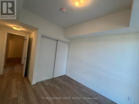 A room with white walls and wooden flooring, with a door on the left and a closet on the right.