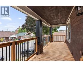 A wooden deck with a black railing and a black car parked in the background.