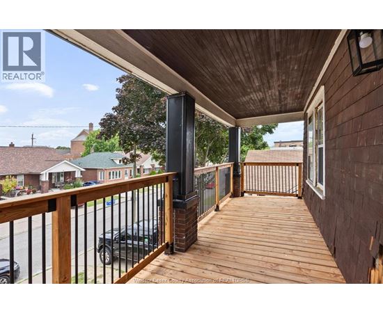 A wooden deck with a black railing and a black car parked in the background.