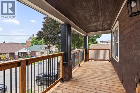 A wooden deck with a black railing and a black car parked in the background.