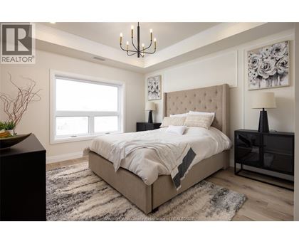 A bedroom with a large bed, a chandelier, and a vase on a side table.