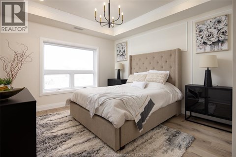 A bedroom with a large bed, a chandelier, and a vase on a side table.