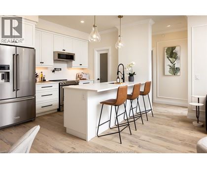 A kitchen with white cabinets and a white island with three chairs.