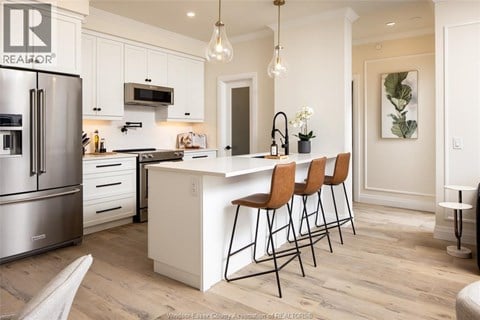 A kitchen with white cabinets and a white island with three chairs.