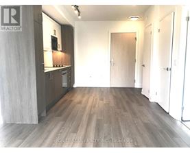 A room with wooden flooring and a kitchen area with white cabinets.