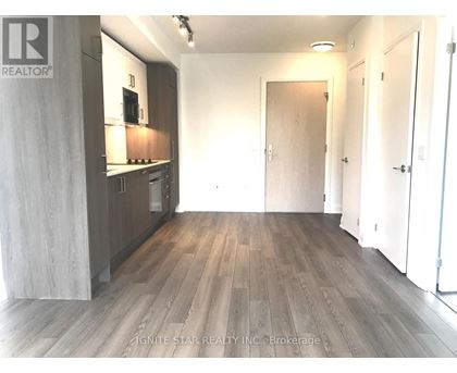 A room with wooden flooring and a kitchen area with white cabinets.