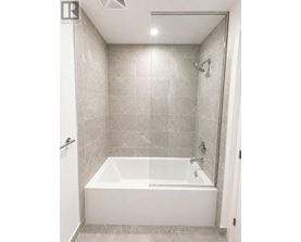 A white bathtub in a bathroom with grey tiles.