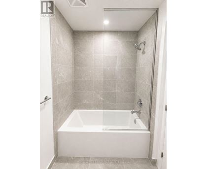 A white bathtub in a bathroom with grey tiles.