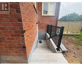 A brick wall with a black railing and steps leading up to a window.