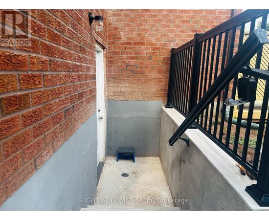 A brick wall with a black railing and steps leading up to a window.