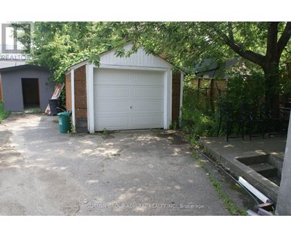 A garage with a white door is surrounded by trees and has a concrete driveway.