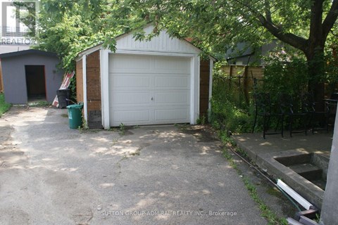 A garage with a white door is surrounded by trees and has a concrete driveway.