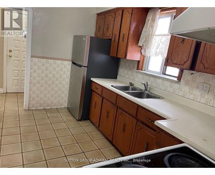 A kitchen with a black fridge, brown cabinets and a tiled floor.