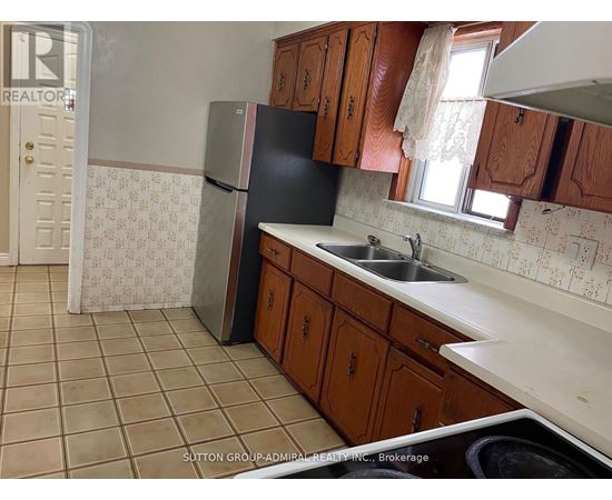 A kitchen with a black fridge, brown cabinets and a tiled floor.