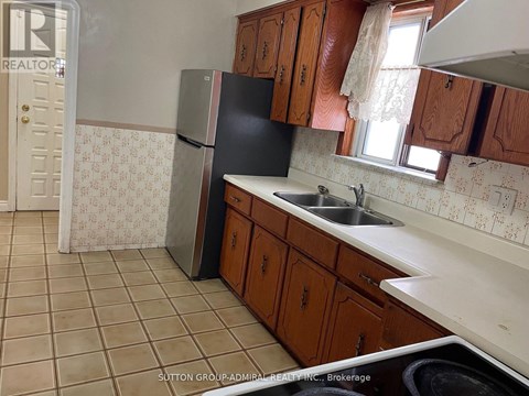 A kitchen with a black fridge, brown cabinets and a tiled floor.