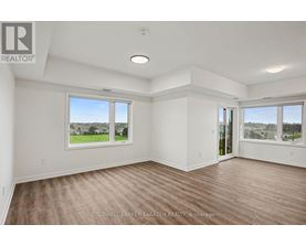 A spacious room with wooden flooring and large windows overlooking a green landscape.