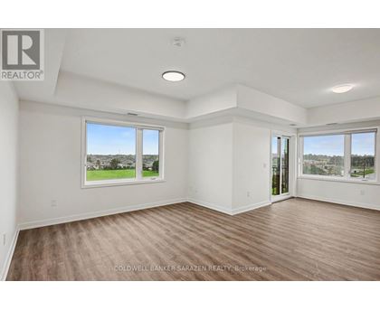 A spacious room with wooden flooring and large windows overlooking a green landscape.