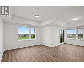 A spacious room with wooden flooring and large windows overlooking a green landscape.